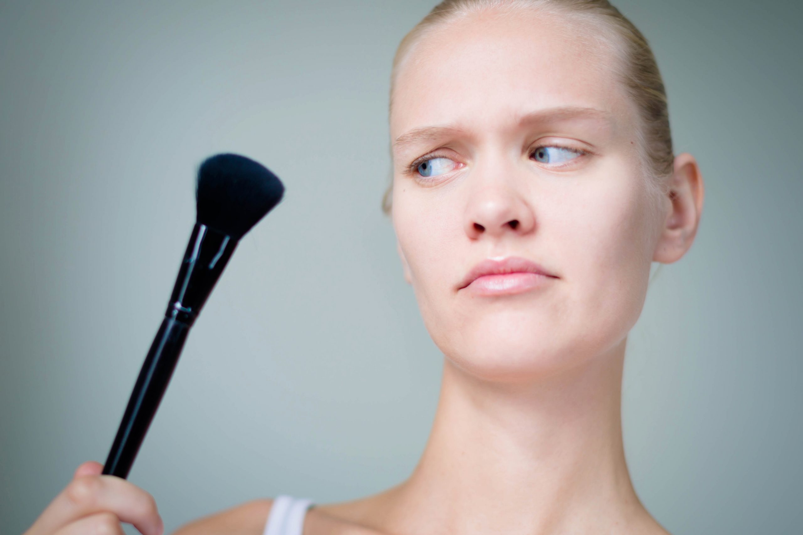 Woman looking suspiciously at makeup brush that may be dirty